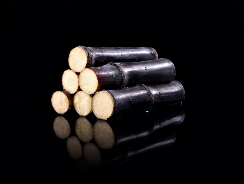 Freshly cut lengths of purple sugarcane showing their pale, juicy centres, lit against black